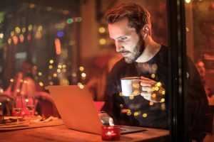 A young man drinking coffee while reading online reviews about long distance movers NJ on his laptop