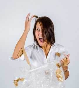 An irritated woman with packing supplies, trying to get tape out of her hair.