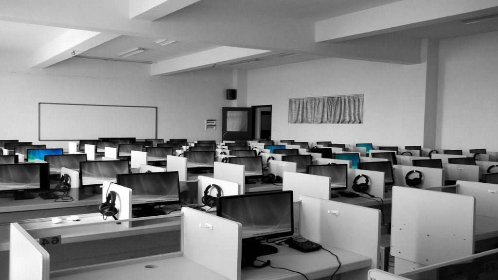 Modern office space - many white desks with computers and headsets.