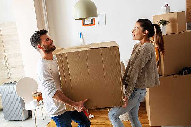 A young man and a young woman in their apartment, holding a big box together