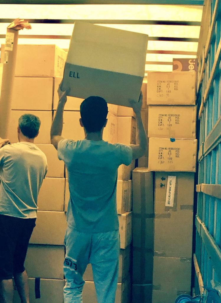 Two male Essex County movers lifting boxes in a storage unit full of boxes