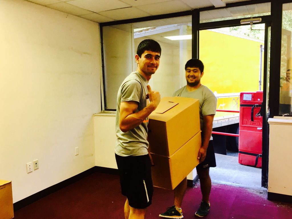 Two Hoboken movers holding a large box, smiling