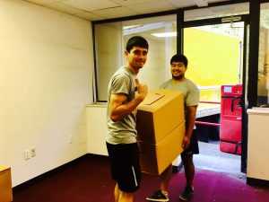 Two Hoboken movers holding a large box, smiling