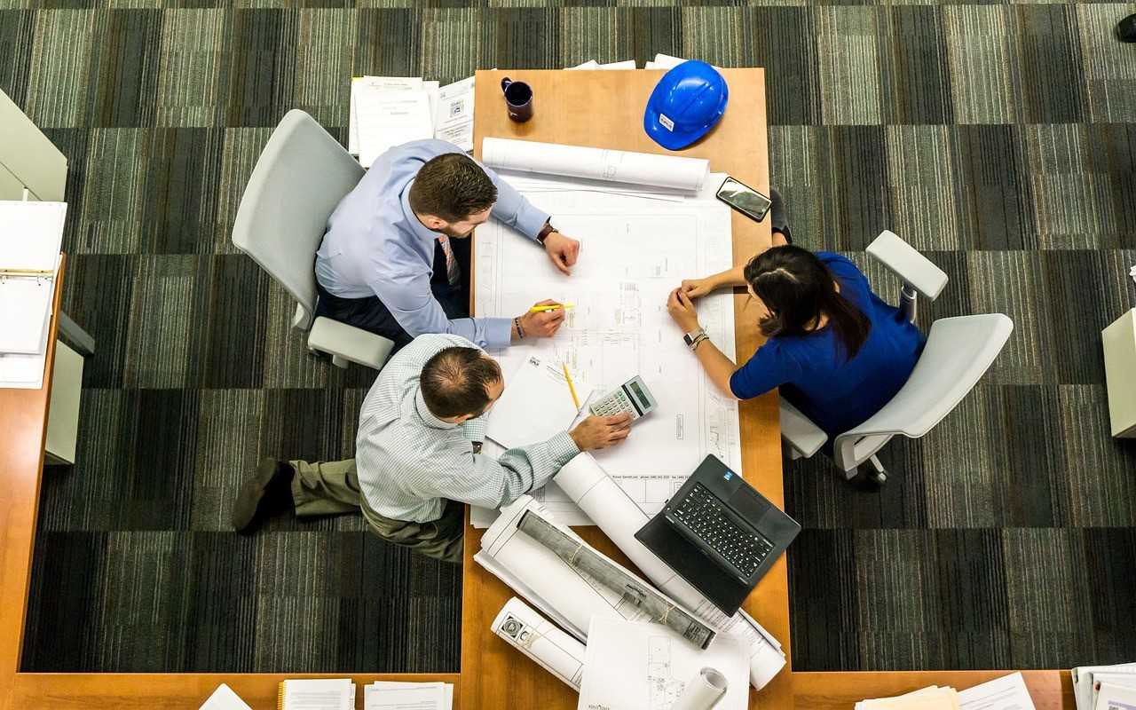 Office interior, three people sitting at a large desk full of papers