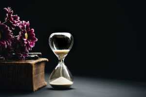 Hourglass next to a large book, with purple flowers on it (black background).