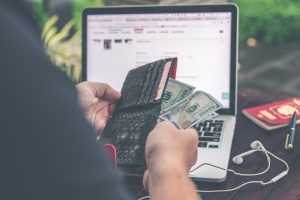 A person taking money from a wallet, a laptop in the background