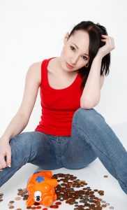 A young woman with money problems, planning to claim moving expenses, a piggy bank and some metal coins in front of her