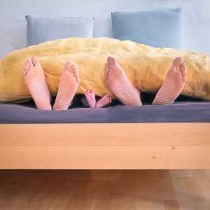 Three pairs of feet sticking from under a blanket