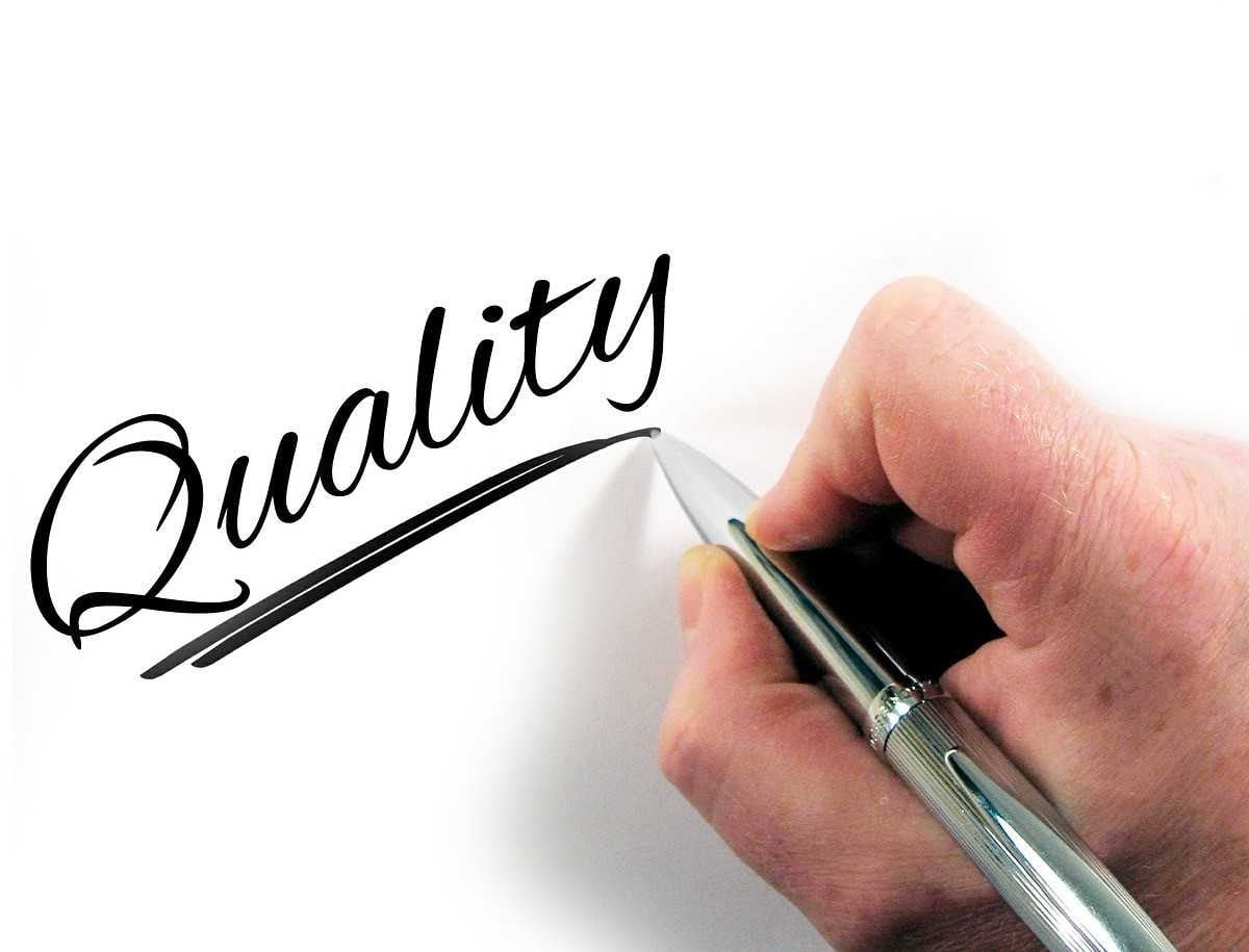A hand writing the word quality on a white surface
