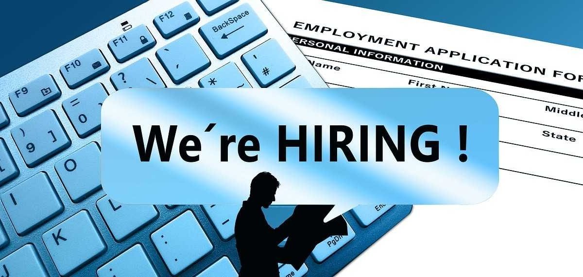 A male silhouette holding newspapers, "We're hiring" written across the picture, a keyboard and an employment application form in the background