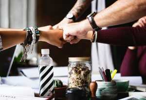 Friends bumping fists, a table with a jar a bottle and other small items underneath them